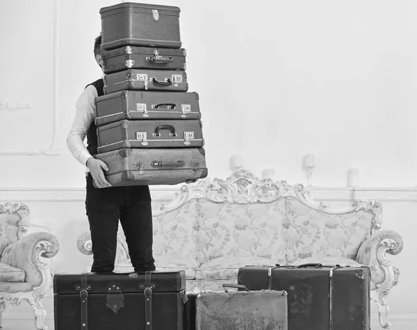 Butler en service concept. Macho, elegante porter draagt zware stapel vintage koffers. Man met baard en snor dragen van klassieke pak levert bagage, luxe witte interieur achtergrond — Stockfoto