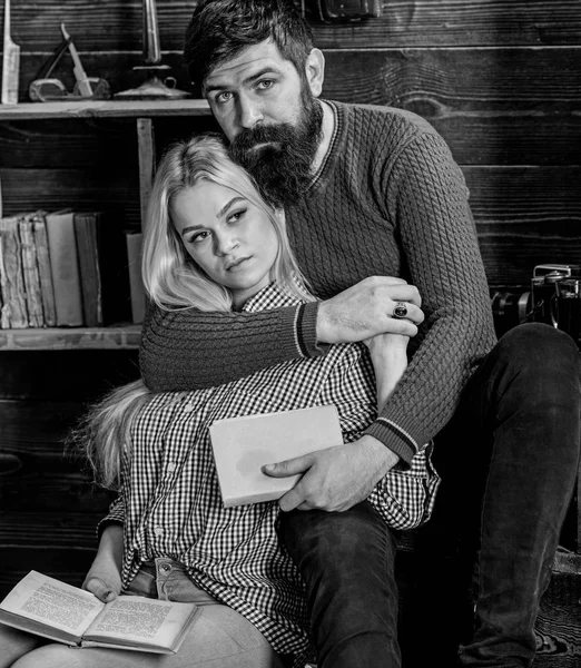 Romantic evening concept. Lady and man with beard on dreamy faces hugs and reading romantic poetry. Couple in wooden vintage interior enjoy poetry. Couple in love reading poetry in warm atmosphere