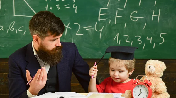 父は、息子の数学を教えています。正式な摩耗と鏝板の教室で、背景に黒板に生徒の教師。演算に関するレッスンのコンセプトです。陽気な子供の先生と勉強 — ストック写真