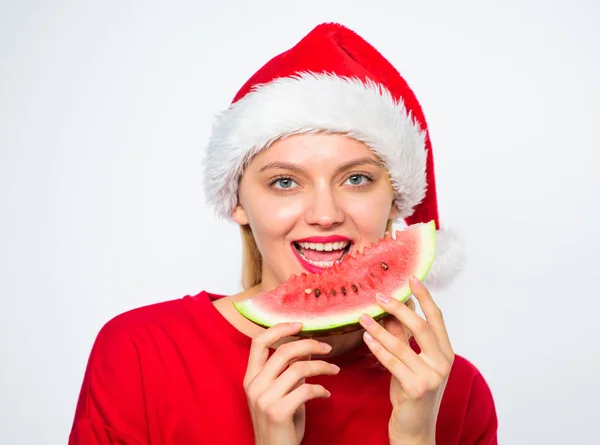 圣诞女孩吃西瓜。异国情调的寒假。女孩戴圣诞老人帽子吃切片西瓜白色背景。庆祝新年的夏天。夏天在圣诞晚会上举行。异国情调的圣诞节概念 — 图库照片