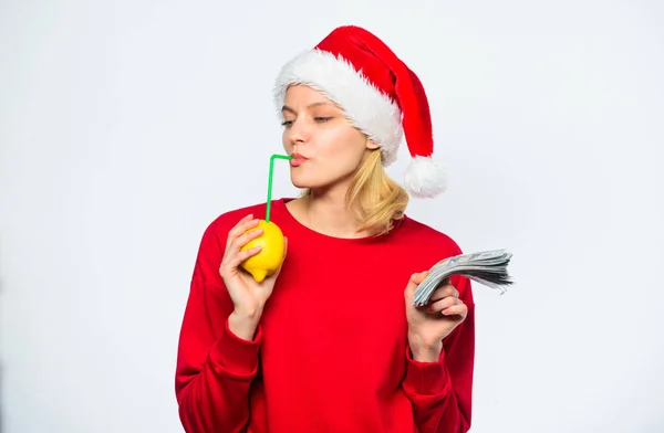 Tyttö jouluhattu juoda mehua sitruuna olki samalla pitää kasa rahaa. Vaurauden ja vaurauden symboli. Joulutoiveita. Rikas tyttö, jolla on sitruunaa ja rahaa. Sitruunamiljonääri. Sitruunarahan käsite — kuvapankkivalokuva