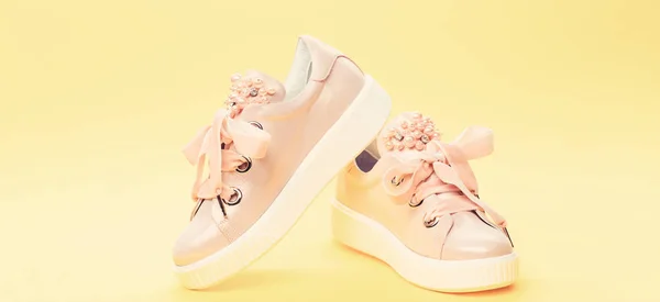 Comfortable footwear concept. Cute shoes on yellow background. Footwear for girls or women decorated with pearl beads. Pair of pale pink female sneakers with velvet ribbons — Stock Photo, Image