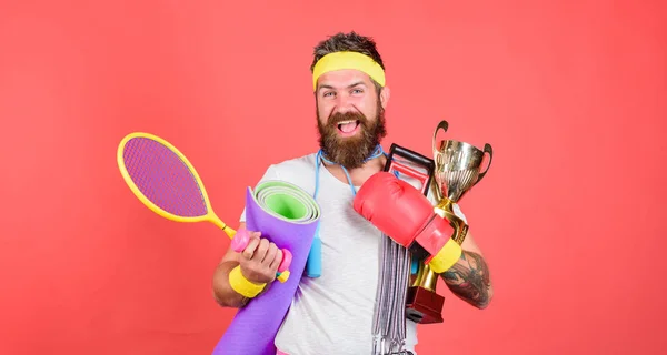 Sport lifestyle concept. My goal is health. Sport shop assortment. Man bearded athlete hold sport equipment jump rope fitness mat boxing glove expander racket and golden goblet. Choose sport you like