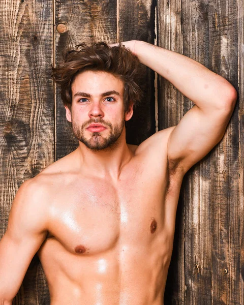 Guy seductive glance shimmering skin. Sexy attractive macho tousled hair on wooden background. Sportsman show six pack sexy torso. Bachelor sexy body chest and belly. Man athlete with fit torso