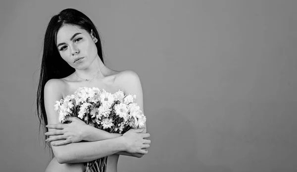 Woman hiding her breasts, covers with bouquet. Cancer of breast concept. Lady covers breasts with flowers, grey background. Girl on calm face naked holds chamomile flowers in front of chest