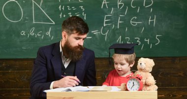 İlk öğretim. Baba oğul, öğretir tartışmak, açıklamak. Eğitim kavramı. Öğretmen ile eğitim evlat. Öğretmen formal giyim ve öğrenci sınıfta kolej, kara tahta arka plan