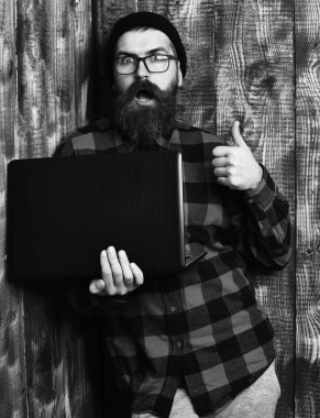 Sakallı adam, uzun sakal. Acımasız beyaz sürpriz tıraşsız hipster dizüstü şapka ve gözlük kahverengi vintage ahşap studio adam kırmızı siyah damalı gömlek holding