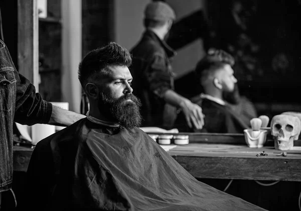 El barbero, un hombre con barba en el proceso de cortar a un cliente en la  barbería, una foto en blanco y negro.