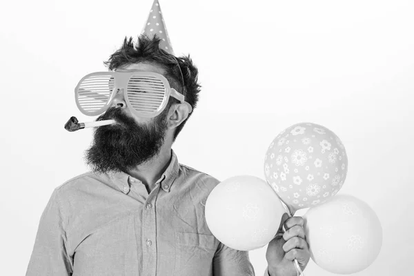 Homem com barba e bigode no rosto calmo contém balões de ar, fundo branco. O tipo de chapéu de festa com chifre de festa celebra. Conceito de festa. Hipster em óculos de sol gigantes celebrando aniversário — Fotografia de Stock
