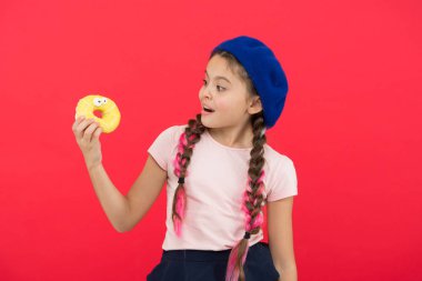 Pişmiş Donuts büyük fanlar çocuklar. Resist taze yapılmış çörek için imkansız. Kız tatlı çörek elinde kırmızı camlı arka plan tutun. Çocuk gülümseyen kız donut yemeye hazır. Şeker dükkanı ve ekmek kavramı