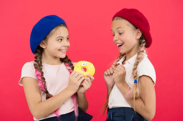 I bambini ammirano molto le ciambelle al forno. Condividi ciambella dolce. Ragazze in berretto cappelli tenere smaltato ciambella sfondo rosso. Bambini ragazze giocose pronto mangiare ciambella. Amicizia e generosità. Dolci negozio e panetteria concetto — Foto Stock