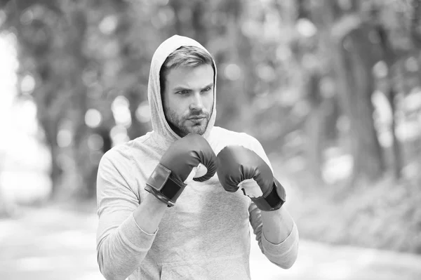 Boxer exercise on fresh air. Knowckout. Man punching. Fight for success. Man in boxing gloves and hood on natural landscape. Training his boxing skills. Born to fight. Power and energy