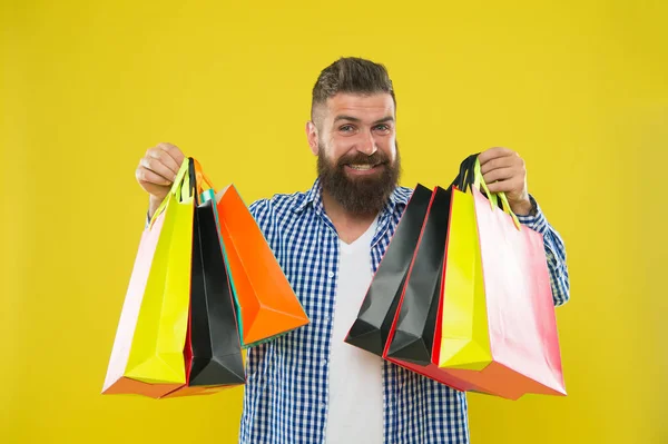 Uomo barbuto hipster faccia allegra portare borse della spesa di carta su sfondo giallo. Godetevi lo shopping offerte redditizie venerdì nero. Shopping con sconto godere di acquisto. Rendere lo shopping più gioioso — Foto Stock