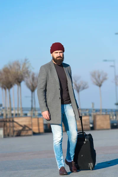 Business trip. Man bearded hipster travel with big luggage bag on wheels. Let travel begin. Traveler with suitcase waiting transportation to airport railway station. Ready to travel. Carry travel bag