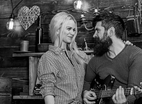 Romantic evening concept. Couple in love spend romantic evening in warm atmosphere. Couple in wooden vintage interior enjoy guitar music. Lady and man with beard on happy faces hugs and plays guitar