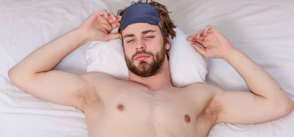 Man stretching in bed. A young man waking up in bed and stretching his arms. Man hand under blanket reaching out for alarm clock on holiday.