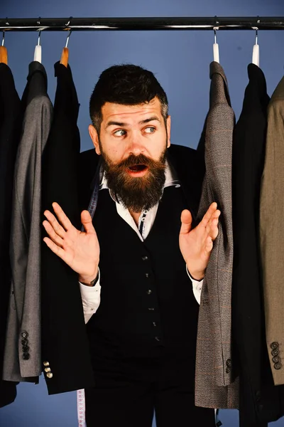 Asistente de tienda o vendedor se esconde entre trajes en perchas de ropa. — Foto de Stock
