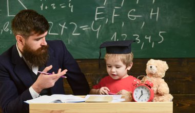 Öğretmen ile eğitim evlat. Baba oğul, öğretir tartışmak, açıklamak. Eğitim kavramı. İlk öğretim. Öğretmen formal giyim ve öğrenci sınıfta kolej, kara tahta arka plan