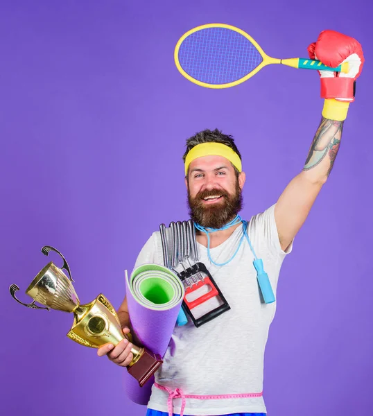 On way to achievement. Sport shop assortment. Man bearded athlete hold sport equipment jump rope fitness mat boxing glove expander racket and golden goblet. Choose favorite sport. Sport concept