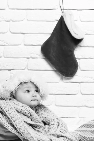 Mały chłopiec z uroczą ciekawą twarzą w żółtym swetrze w nowym roku kapelusz i dzianiny szalik z Boże Narodzenie lub Boże Narodzenie pończochy lub buty na białej cegły tle ściany — Zdjęcie stockowe