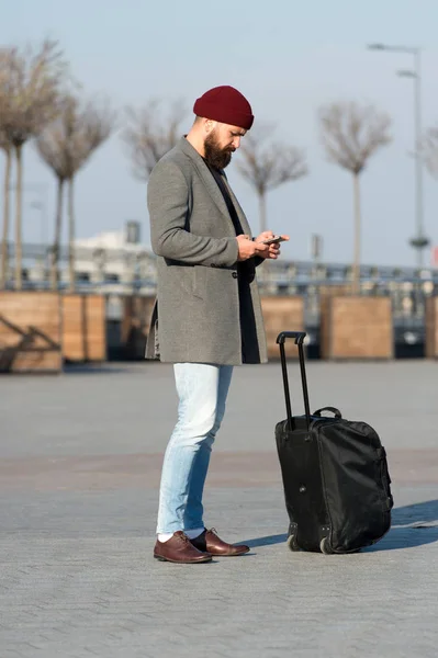 Let travel begin. Traveler with suitcase waiting transportation to airport railway station. Ready to travel. Carry travel bag. Business trip. Man bearded hipster travel with big luggage bag on wheels