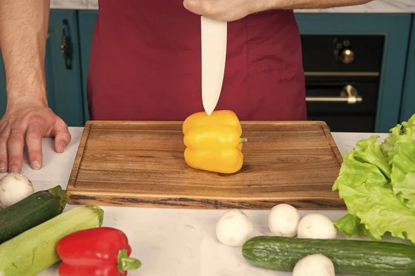 Рука вирізає жовтий перець з ножем на дерев'яній обробній дошці — стокове фото