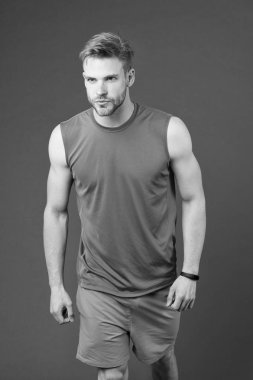 Seksi kaslı vücutlu bir sporcu. Maraton, spor ve spor konseptinden önce koşuculuk eğitimi. Süslü sakallı, turuncu yelek ve mavi şort giyen bir adam. Sporcu mor arkaplanda izole edildi