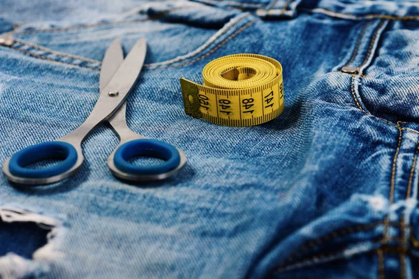 Metal scissors and yellow measure tape on jeans, close up — Stock Photo, Image