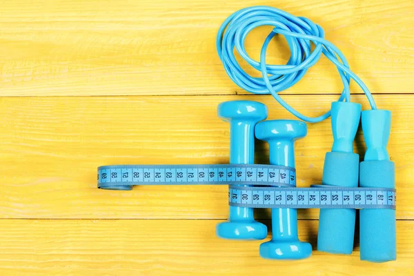 Dumbbells, jump rope, centimeter for weight loss. Fitness tools, blocknote,  pen and apple on brown wooden background. Gym and healthy lifestyle  concept. Sports equipment in cyan blue color, top view Stock Photo 