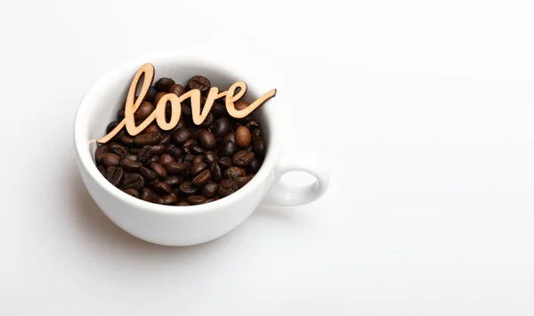 Filiżanka ceramiczna z ziaren kawy i drewniane słowo miłość. Romantyczny przerwa na kawę. Ziarna kawy kubek na białym tle. Ciesz się pić kawę. Data w café koncepcja. Napój składają się kofeiny — Zdjęcie stockowe