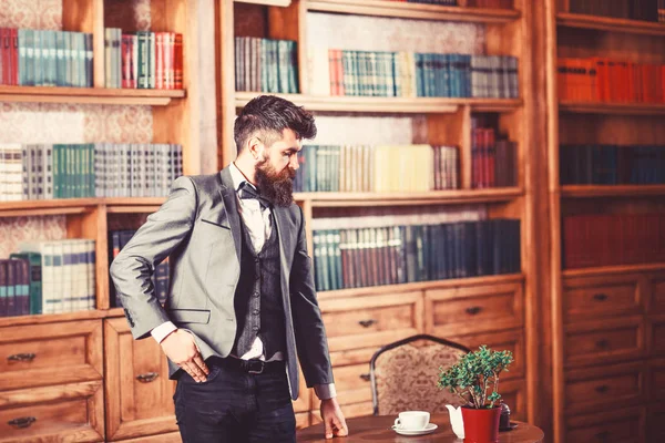 Law, advocacy, professional success, vintage concept. Lawyer stands in vintage interior near table with cup of tea or coffee. Bearded man in elegant suit in his cabinet. Avocat with thoughtful face