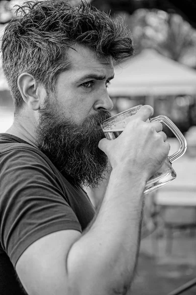 Homme à la barbe et à la moustache tient un verre avec de la bière tout en se relaxant sur la terrasse du café. Le type se repose avec de la bière fraîche. Hipster sur le visage calme buvant de la bière en plein air. Concept de bière Draught — Photo