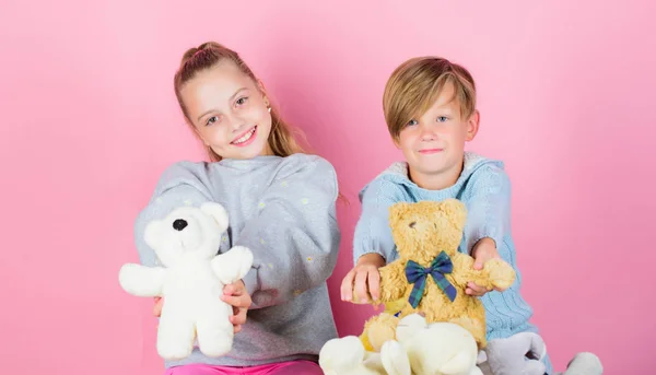 Boy and girl play with soft toys teddy bear on pink background. Bears toys collection. Teddy bears help children handle emotions and limit stress. Siblings playful hold teddy bear plush toys