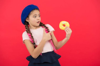 Şeker dükkanı ve ekmek kavramı. Pişmiş Donuts büyük fanlar çocuklar. Resist taze yapılmış çörek için imkansız. Kız tatlı çörek elinde kırmızı camlı arka plan tutun. Çocuk oynak kız donut yemeye hazır