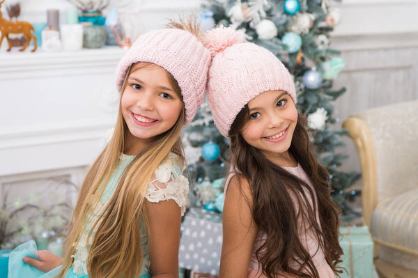 Модные девчонки. Аксессуар зимнего сезона. Дети носят вязаные шляпы. Девушки длинные волосы счастливые улыбающиеся лица рождественский фон елки. Дети носят теплые мягкие вязаные розовые шляпы. Модные вязаные шляпы для девочек
