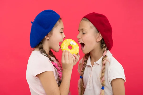 Douce vie. Boutique de bonbons et concept de boulangerie. Les enfants fans de beignets cuits au four. Partager donut sucré. Les filles dans les chapeaux de béret tiennent beignet fond rouge. Les enfants filles ludiques prêt à manger beignet. Amitié et générosité — Photo