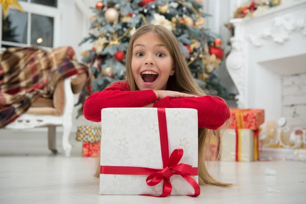圣诞节就要到了。可爱的小女孩收到了节日礼物。最好的圣诞礼物孩子小女孩在优雅的礼服和礼品盒圣诞树背景。孩子为打开她的礼物而兴奋 — 图库照片