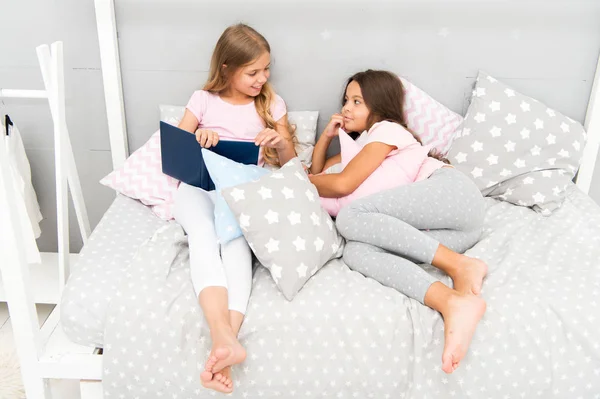 Los niños se preparan para ir a dormir. Agradable tiempo acogedor dormitorio. Las niñas de pelo largo lindo pijama relajarse leer libro. Satisfecho con el libro final feliz. Su libro favorito. niñas hermanas laico cama leer libro juntos —  Fotos de Stock