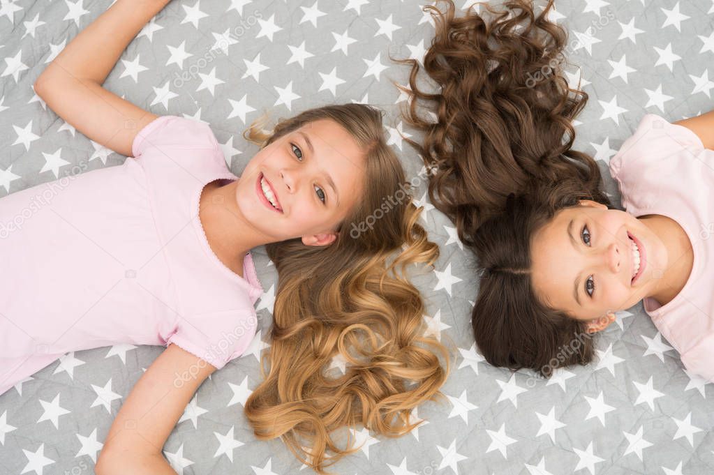 Children curly hairstyle relaxing. Keep hair curly even next morning. Girls children with long hair lay on bed top view. Conditioner mask organic oil keep hair shiny and healthy. Amazing hair tips