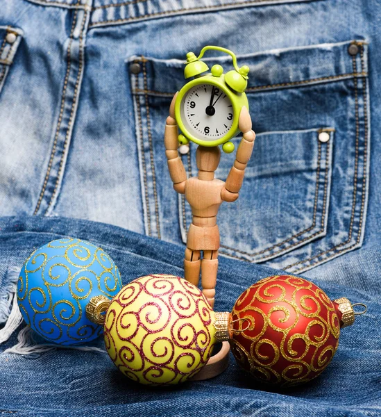 Hračka dřevěný lidské tělo drží hodiny poblíž vánoční dekorace koule. Vánoční dekorativní hračky. Dřevěný model a ornamenty. Vánoční dekorace koncept. Vánoční dekorace džínovina pozadí zblízka — Stock fotografie