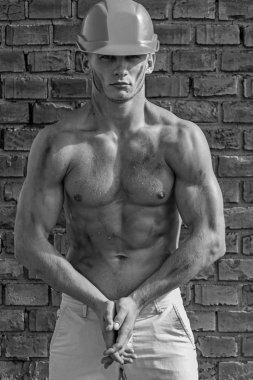 Kask içinde seksi çıplak gövde ile poz atlet. Oluşturucu ile güçlü kas vücut tozla kaplı. Oluşturucu ile kas gövde ve kask, tuğla duvar arka plan üzerinde. Seksi Oluşturucusu kavramı