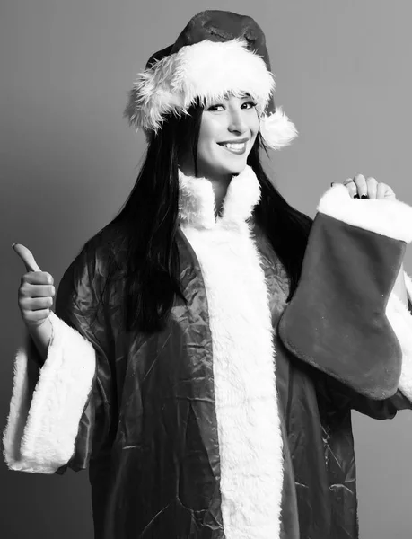 Hoş, seksi Noel Baba kız ya da kırmızı süveter ve yeni yıl şapkalı sırıtan esmer kadın dekoratif noeller, Noel çorapları ya da çizmeler tutuyor ve stüdyo arka planında havalı şeyler gösteriyor. — Stok fotoğraf