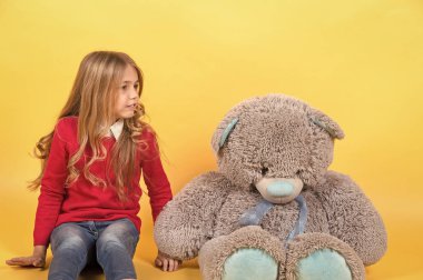 Kız oturup turuncu zemin üzerine büyük oyuncak ayı ile