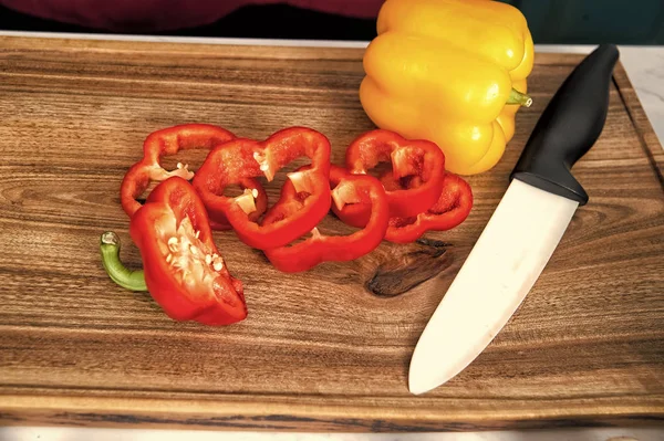 Pepper slices vegetable and ceramic knife on wooden cutting board