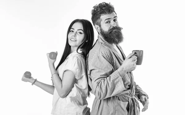 Concept de style de vie alternatif. Couple, famille au visage endormi, pleine d'énergie. Couple amoureux en pyjama, peignoir isolé sur fond blanc. Fille avec haltère, homme avec tasse de café — Photo