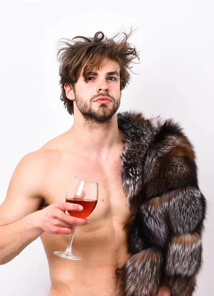 Símbolo de lujo. Estilo de vida y bienestar de lujo. Riqueza y concepto de lujo. Chico atractivo posando abrigo de piel en cuerpo desnudo. Sexy somnoliento macho tousled pelo beber vino o alcohol aislado en blanco — Foto de Stock