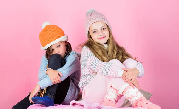 Zatrzymać się w ciepłe i wygodne. Rozgrzać swoje zużycie zimą z akcesoriami ładny i przytulny. Rodzeństwo nosić zimą ciepłe czapki siedzieć na różowym tle. Dzieci chłopiec i dziewczynka rozgrzewkę z swetry i czapki — Zdjęcie stockowe