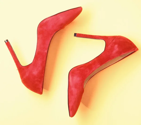 Footwear with thin high heels, stiletto shoes, top view. Shoes made out of red suede on yellow background. Pair of fashionable high heeled pump shoes. Feminine shoes concept