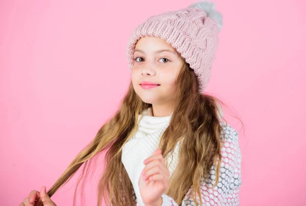 Chica usar sombrero de punto fondo rosa. Prevenir daños en el cabello de invierno. Consejos para el cuidado del cabello de invierno que definitivamente debe seguir. Entrénate en invierno para ir más tiempo entre lavados. Niño pelo largo sonriendo — Foto de Stock