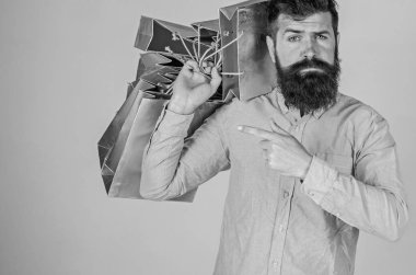 Öneri kavramı. Alışveriş satış sezonu üzerinde adam çanta işaret. Hipster ciddi bir yüz üzerinde satın almak için önerir. Sakal ve bıyık taşır grup alışveriş torbaları, gri arka plan ile adam